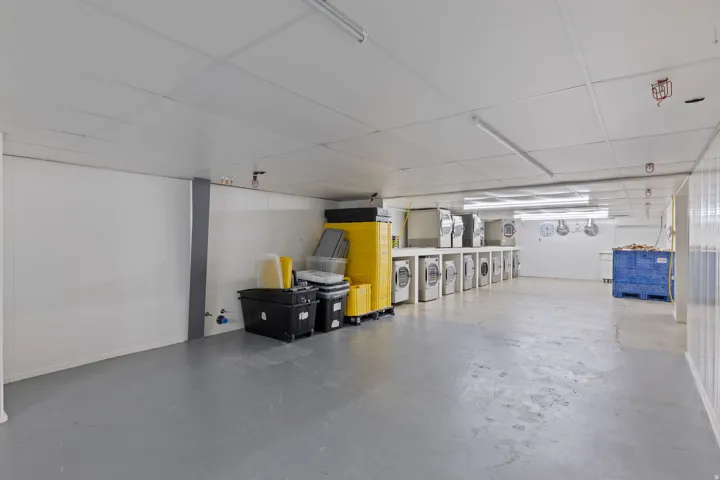Spacious utility room featuring multiple front-load washing machines, built-in shelving, durable flooring, and ample overhead lighting