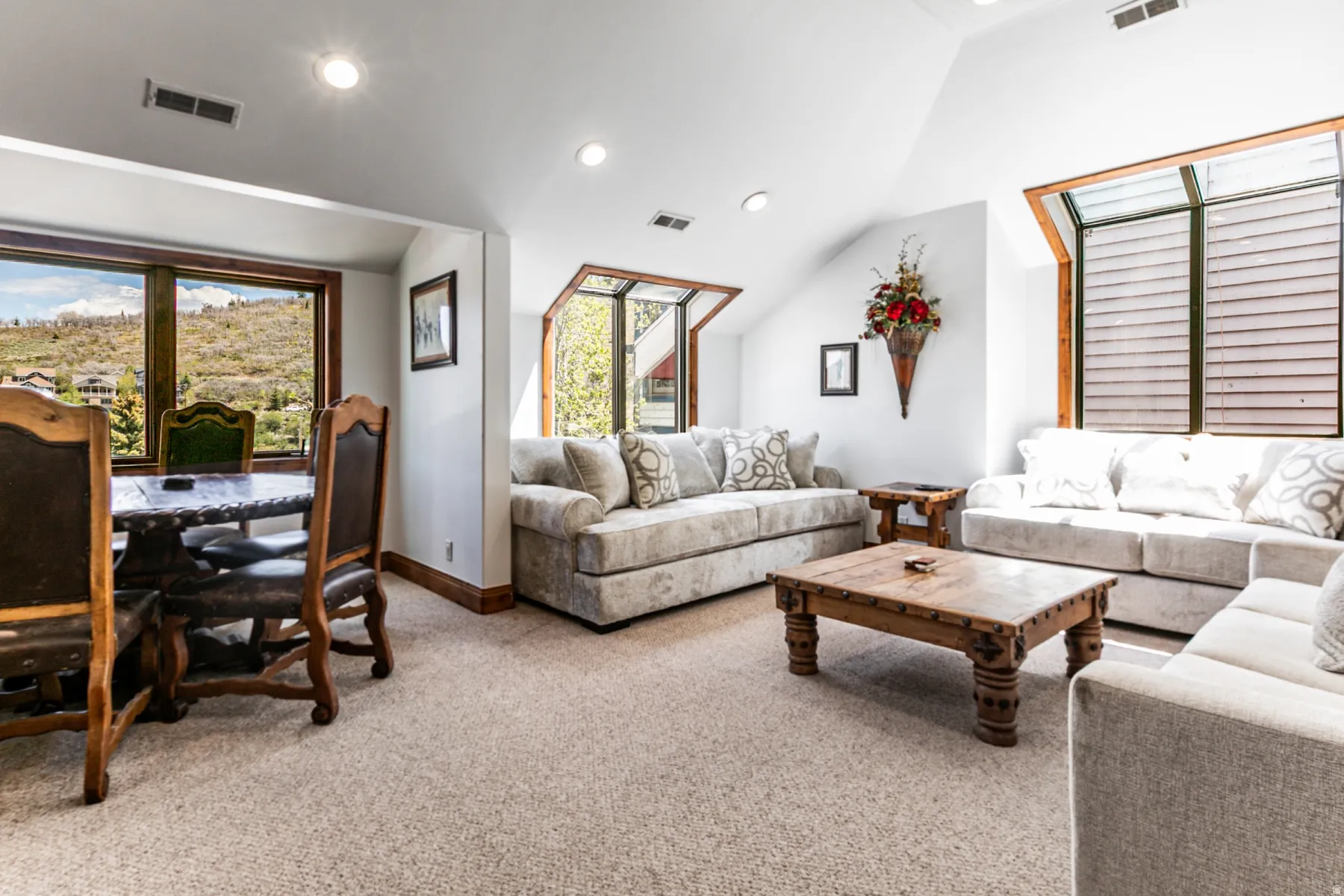 Expansive carpeted living area featuring recessed lighting, multiple windows with wooded frames, and a distinctive angled ceiling