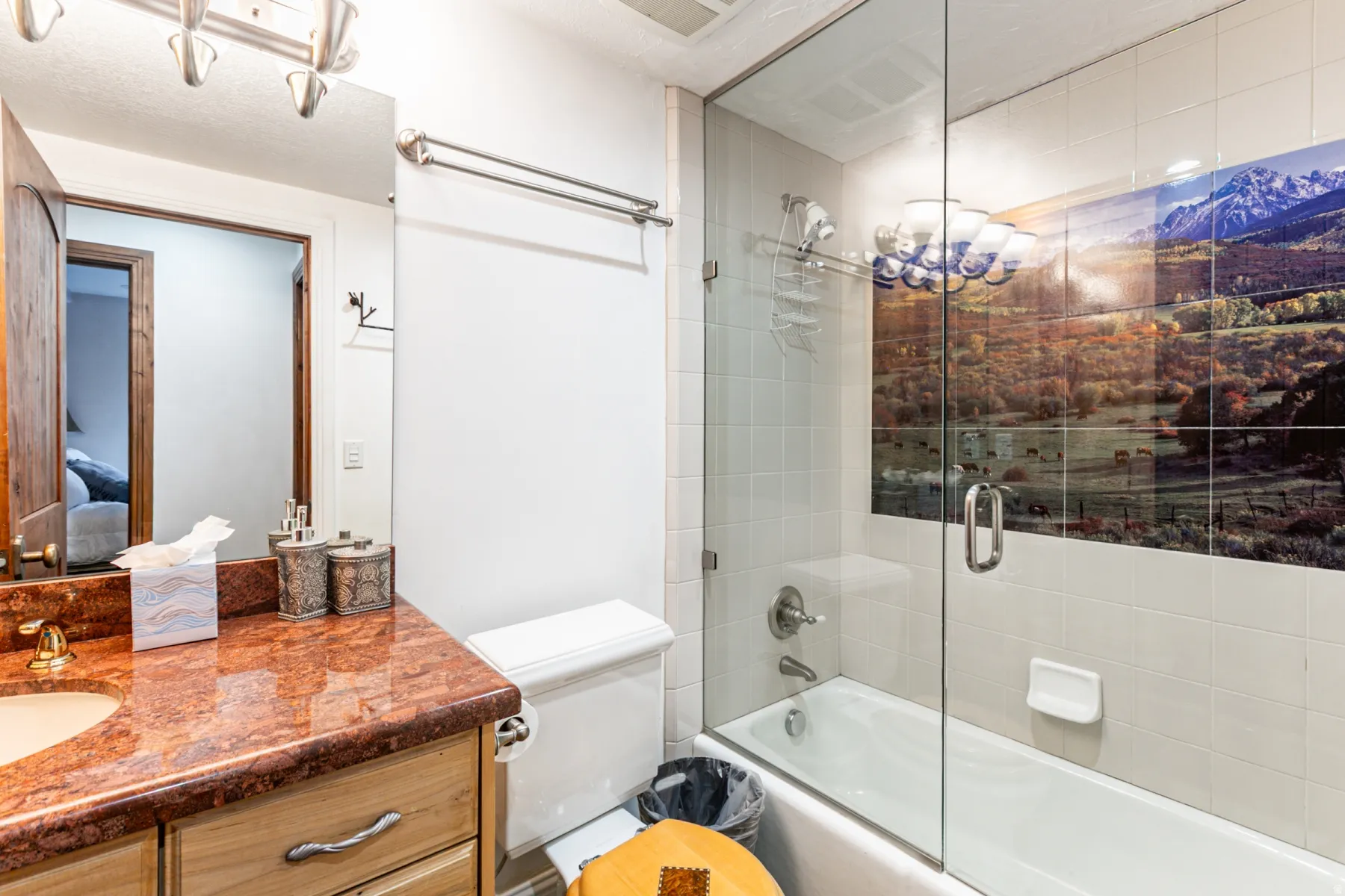 Bathroom featuring a tub/shower combination with a glass enclosure, white square wall tiles, and a decorative landscape tile accent