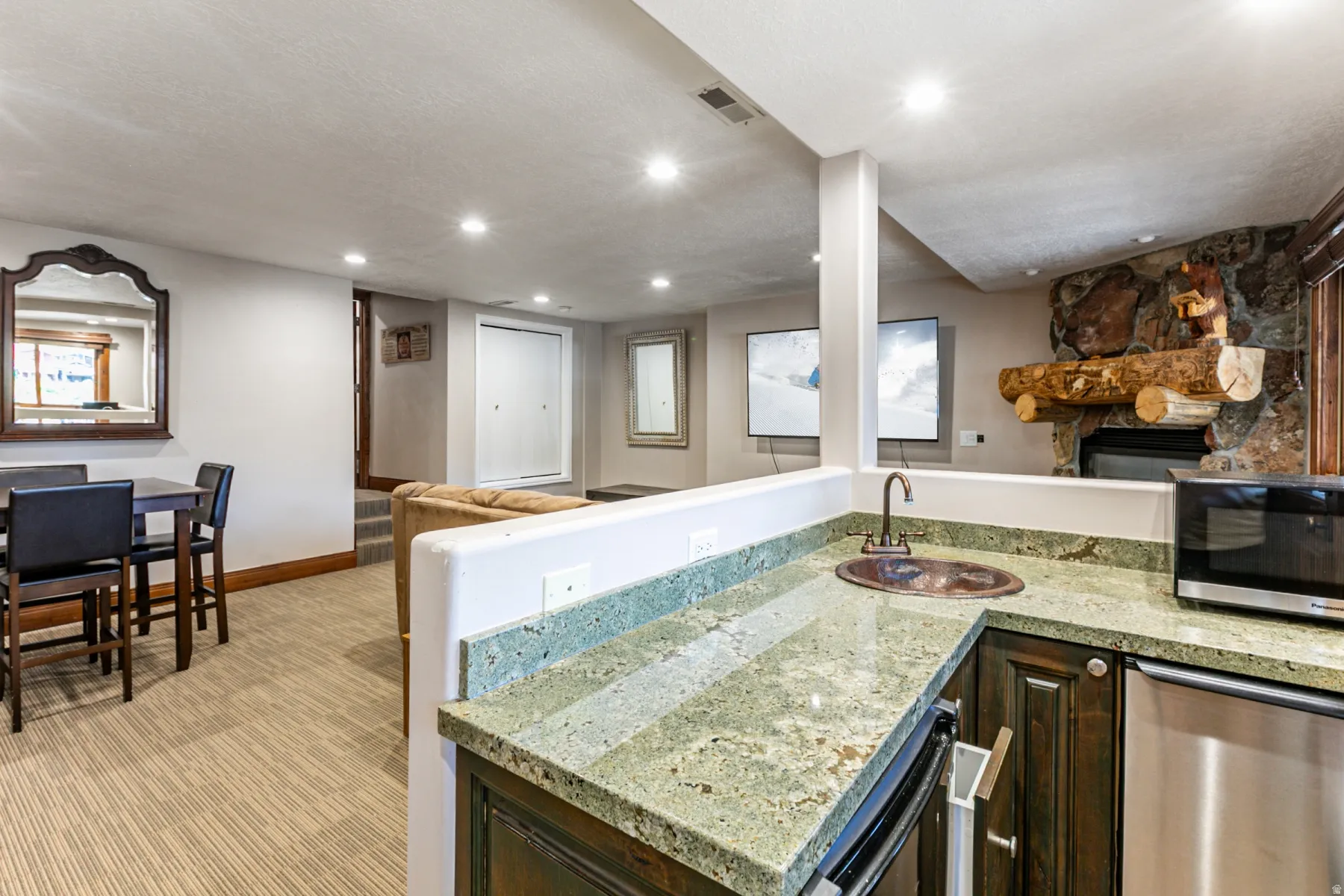 Lower-level entertainment space featuring a stone-faced fireplace with a log mantel, a wet bar with a copper-toned sink, a beverage refrigerator, and recessed lighting