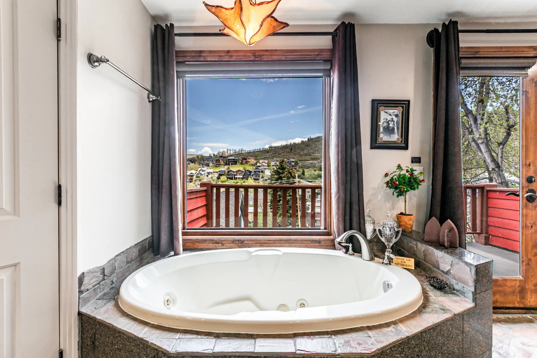 Soaking tub with jetted features, surrounded by a dark stone tile deck and a stone veneer base