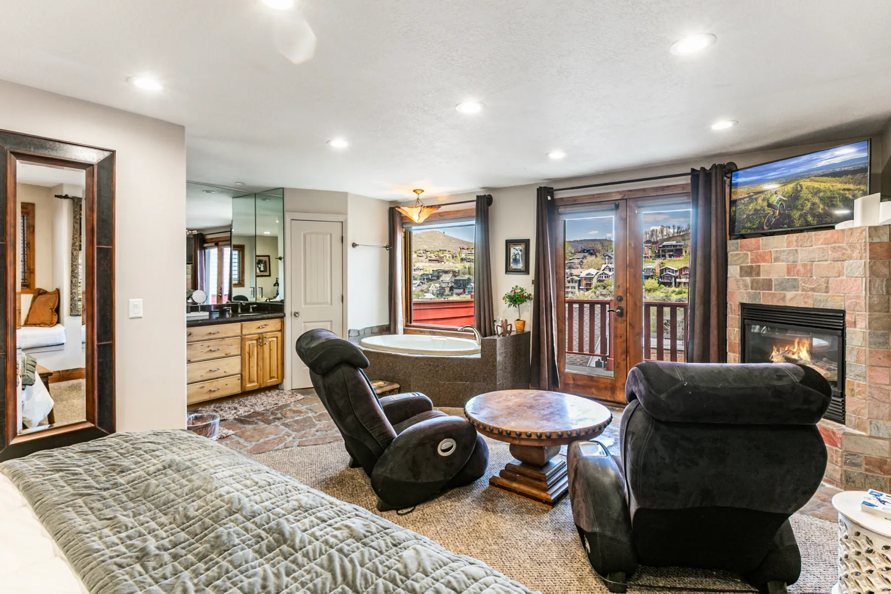 Spacious room featuring a stone-clad fireplace, built-in television, and double doors opening to a balcony