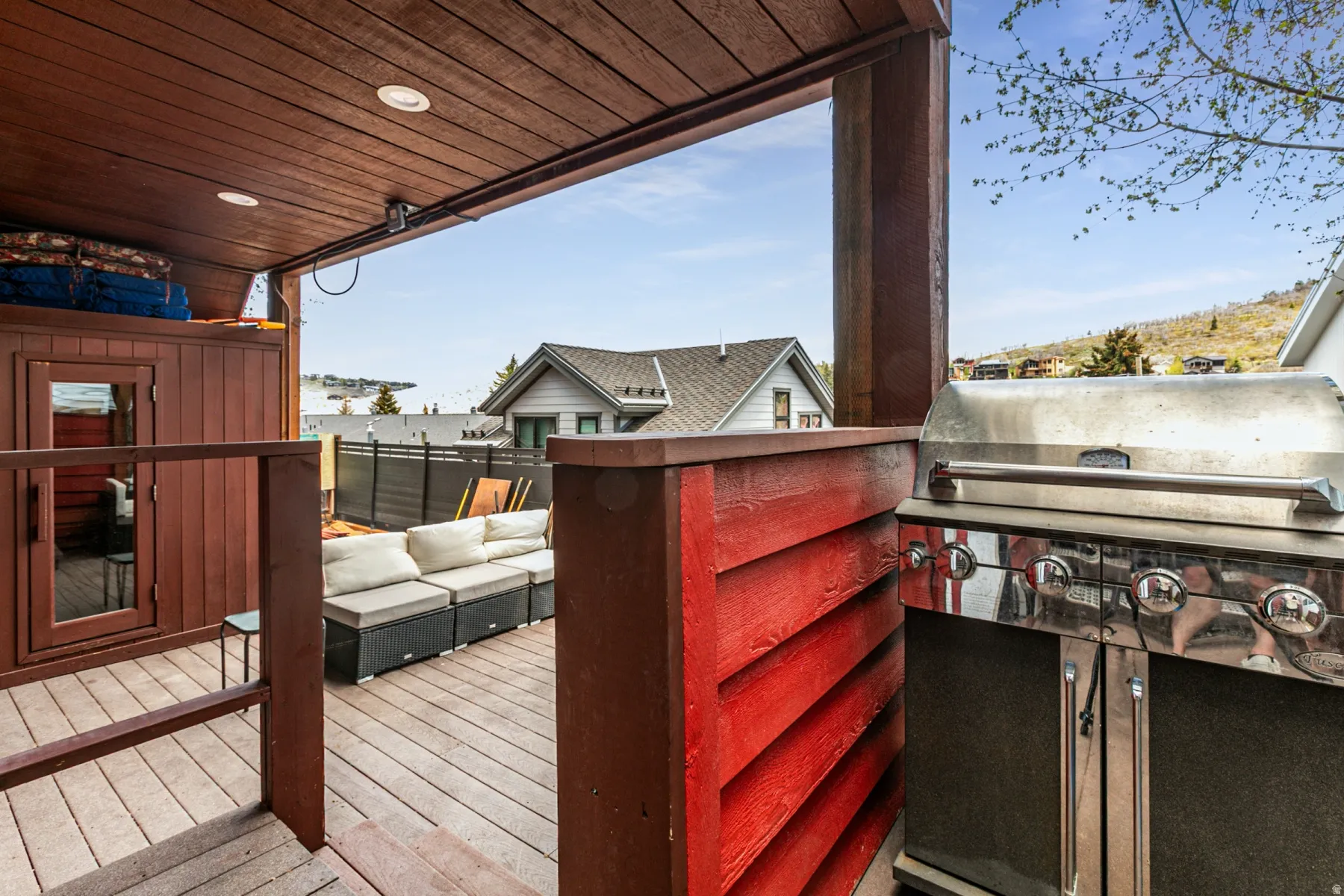 Outdoor deck area featuring wood-finish flooring, a built-in stainless steel grill, and a brown wood-paneled sauna structure with a glass door