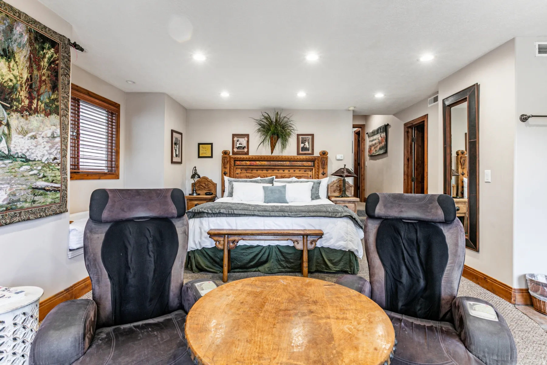 Spacious bedroom featuring recessed lighting, a decorative wood-finish headboard, wood-trim windows with blinds, a full-length wall mirror, and natural wood doors
