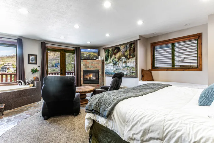 Spacious sleeping area featuring a stone fireplace, recessed lighting, and a large window with wood-finish trim