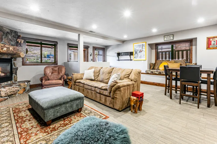 Spacious room featuring a stone-clad fireplace with a wood mantel, recessed lighting, wood-trim windows, and light-toned flooring