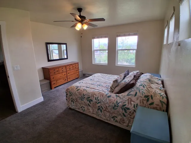 Spacious room featuring neutral painted walls, dark gray carpet flooring, and a ceiling fan with integrated lighting