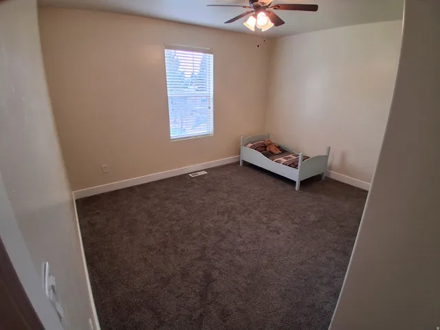 Neutral tone wall paint, dark carpet flooring, and a ceiling fan with integrated lighting