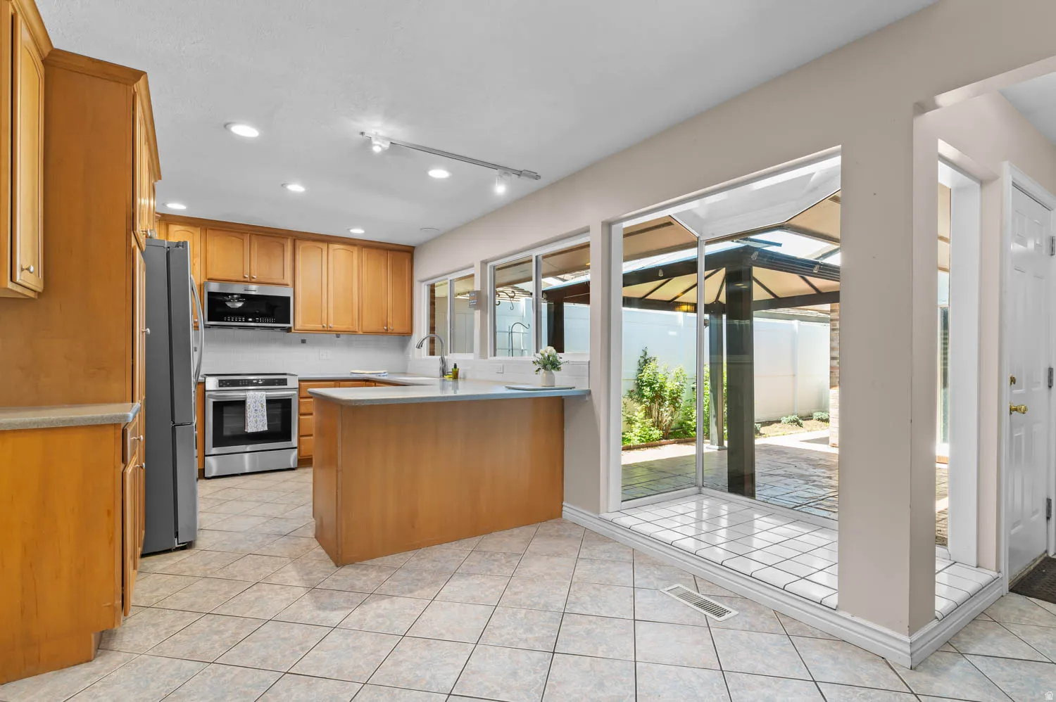 Kitchen featuring light wood cabinetry, stainless steel appliances, a center island with countertop, and large floor tiles