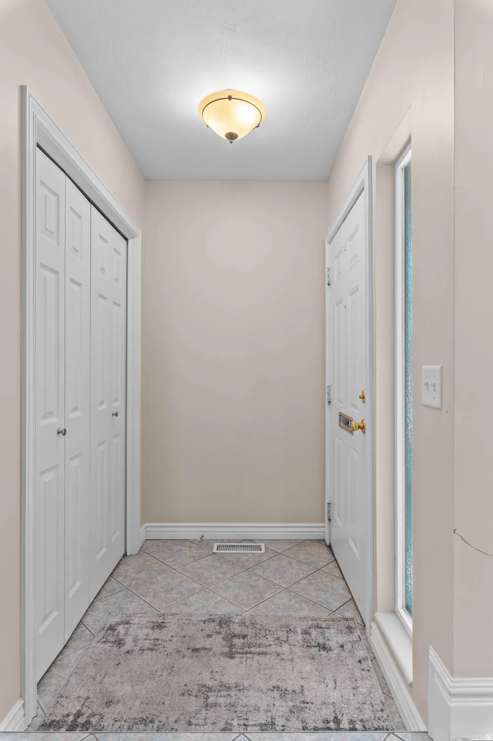 Entryway featuring diamond-set tile flooring, a flush-mount ceiling light fixture, bi-fold closet doors, a paneled entry door with brass hardware, and a sidelight window