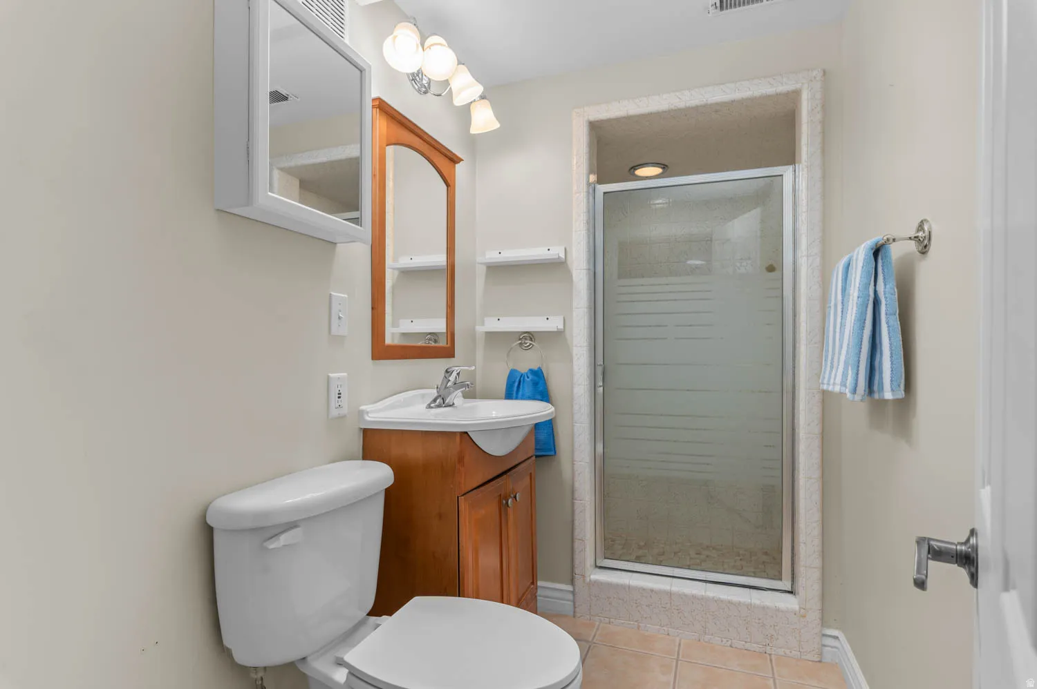 Three-piece bathroom featuring a framed glass-enclosed shower, a vanity with wood-finish cabinetry, a white basin sink, and a toilet