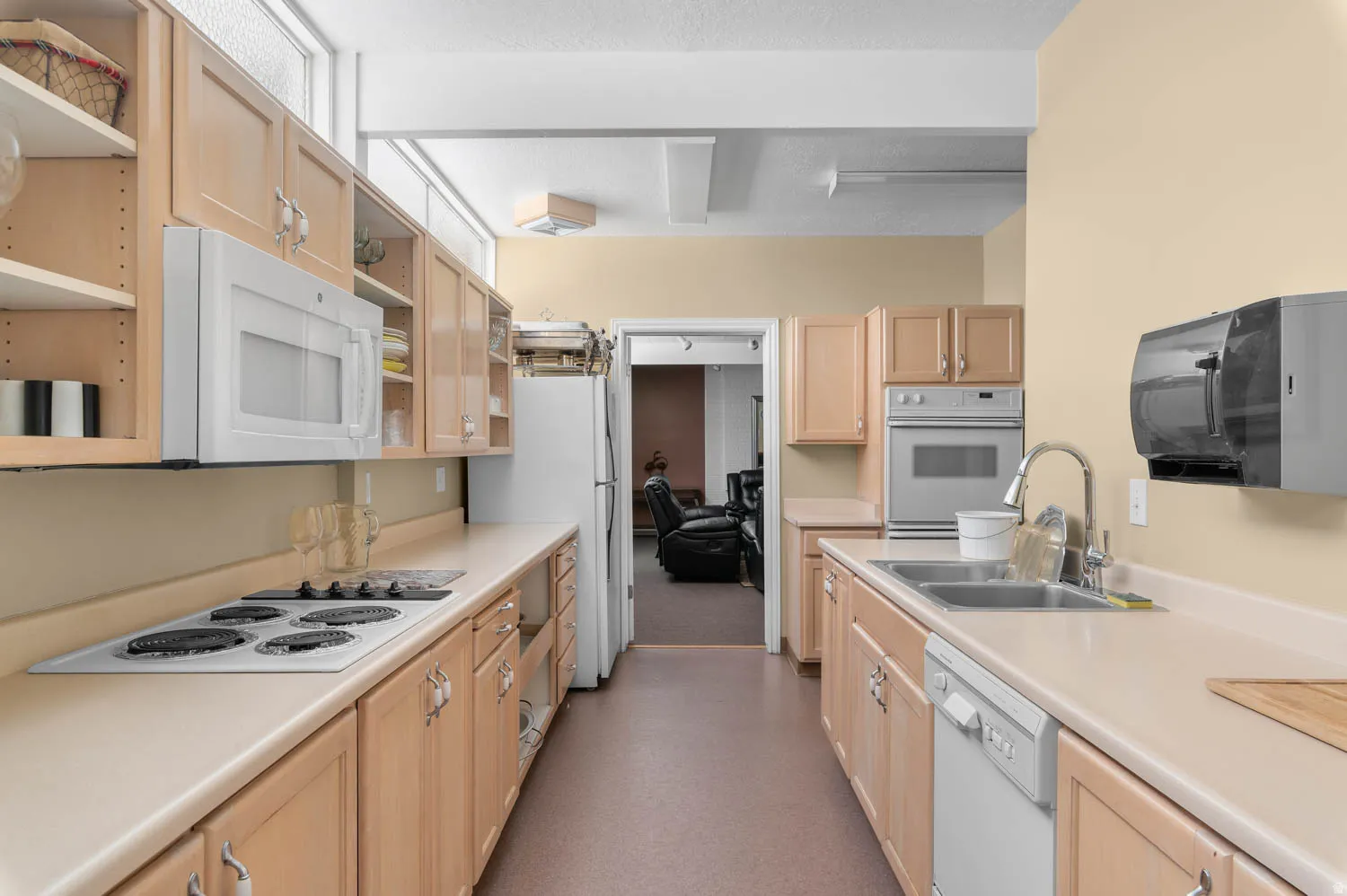 Club House Galley kitchen featuring light wood-finish cabinetry, a built-in electric range, and a double basin stainless steel sink