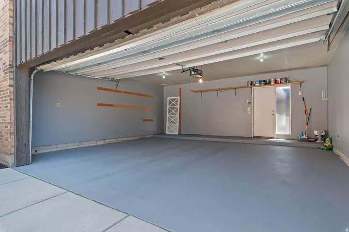 Spacious garage featuring a durable painted concrete floor, overhead lighting, an automatic garage door opener, an interior access door, and wall-mounted shelving