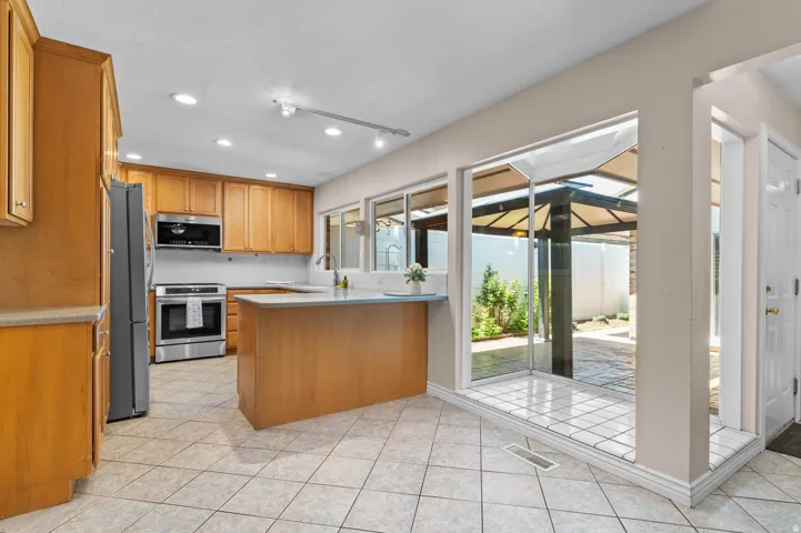 Kitchen featuring light wood cabinetry, stainless steel appliances, a center island with countertop, and large floor tiles