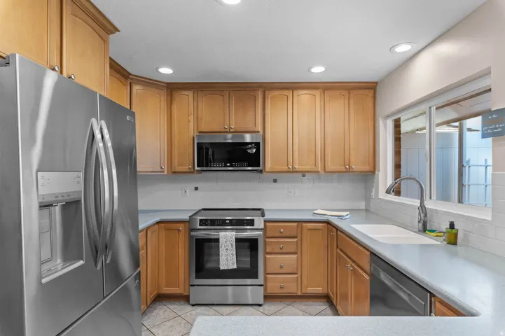 Kitchen featuring wood cabinetry, stainless steel appliances, white subway tile backsplash, and light-toned countertops
