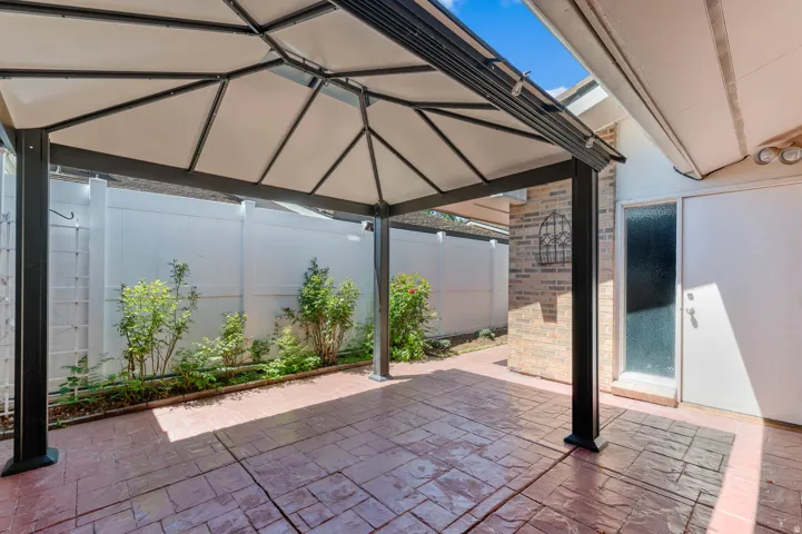 Covered patio with stamped concrete flooring, a privacy fence, and brick exterior accents