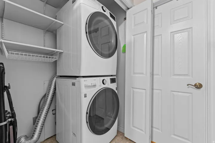 Dedicated laundry area featuring a stacked washer and dryer, white shelving, and a wire storage basket