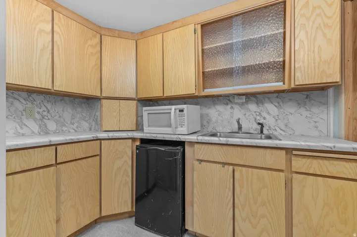 U-shaped kitchen area featuring wood-finish cabinetry, a stainless steel sink, and light-toned countertops with a marbled backsplash