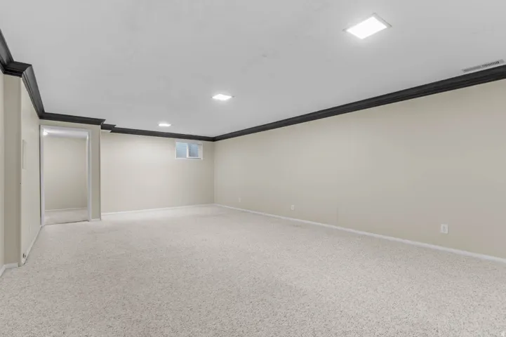 Expansive finished basement featuring light-colored carpeting, neutral wall tones, dark crown molding, and recessed lighting