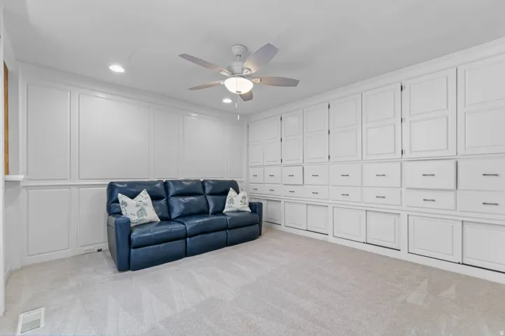 Expansive room featuring extensive built-in cabinetry with flush panel doors and drawers, recessed lighting, ceiling fan, carpet flooring, and wainscoting