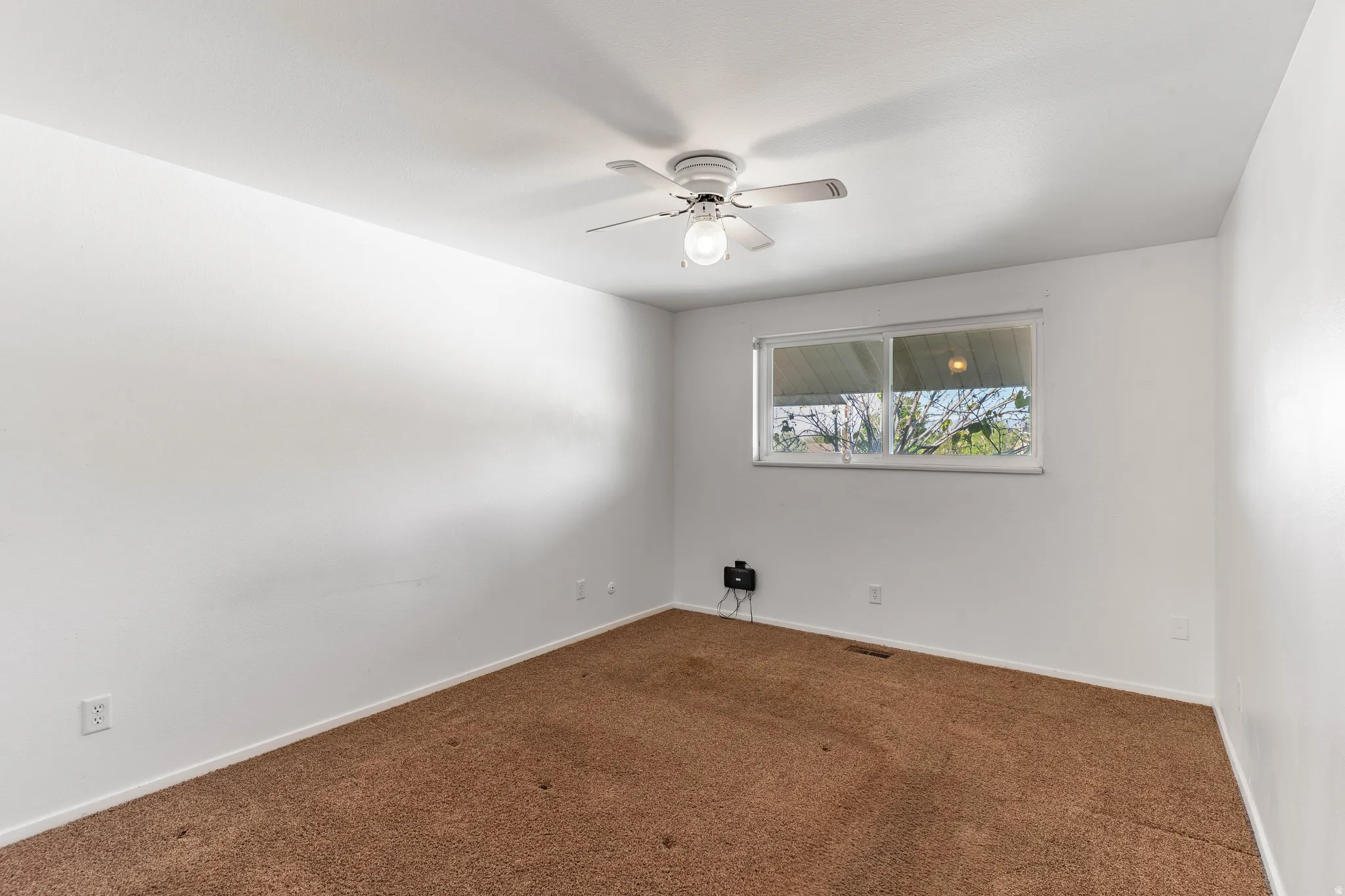 Carpeted room featuring a ceiling fan with light fixture and a double-pane window