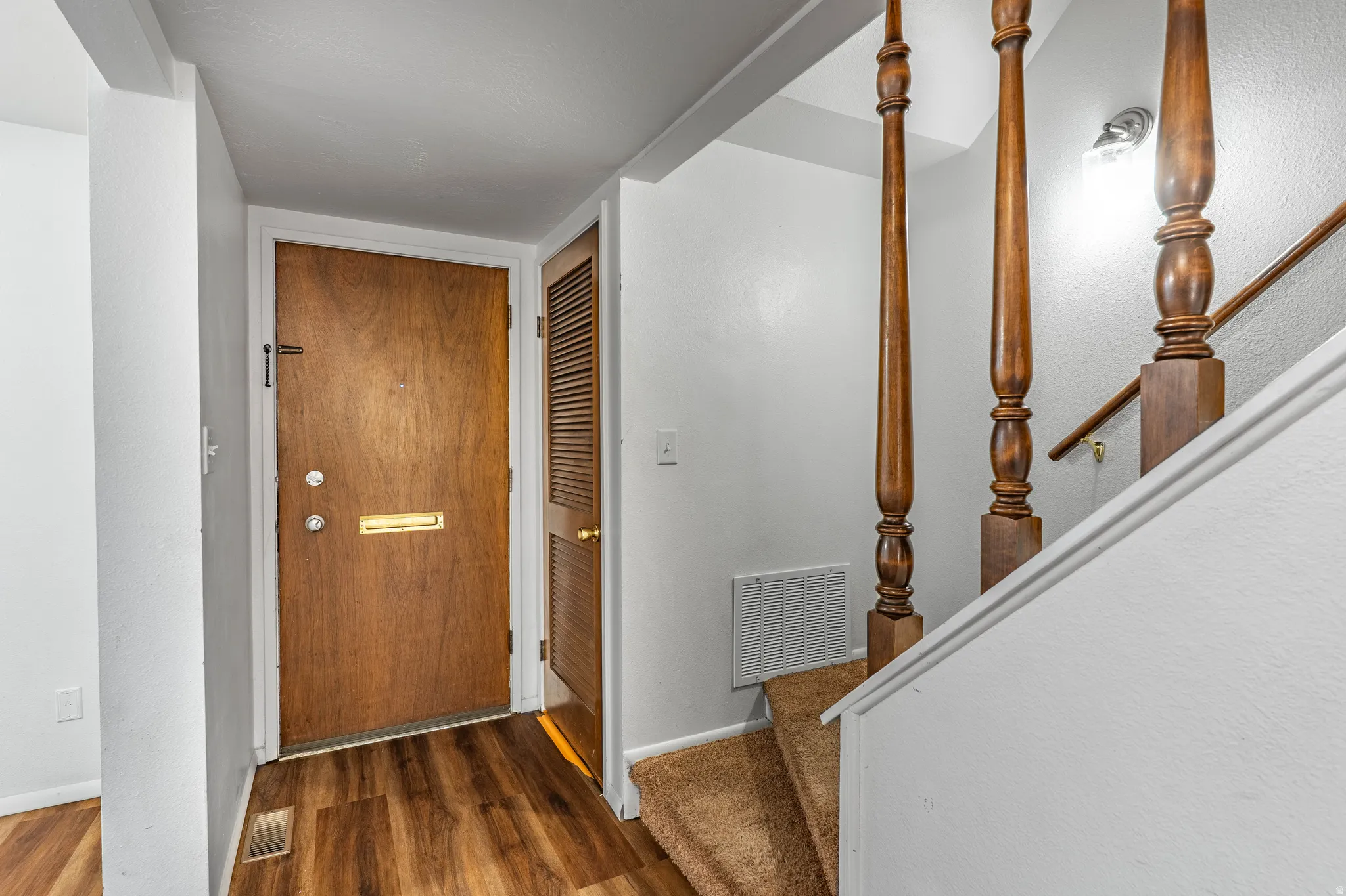 Entryway featuring wood-finish flooring, a solid wood entry door with brass mail slot, and an adjacent louvered door