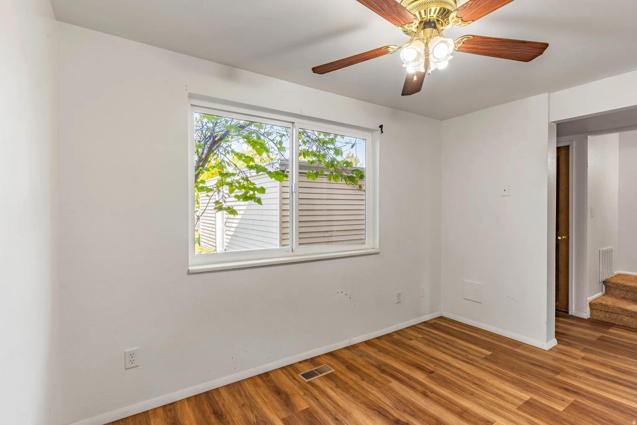Room featuring wood-finish flooring, a double-pane window, and a ceiling fan with integrated lighting