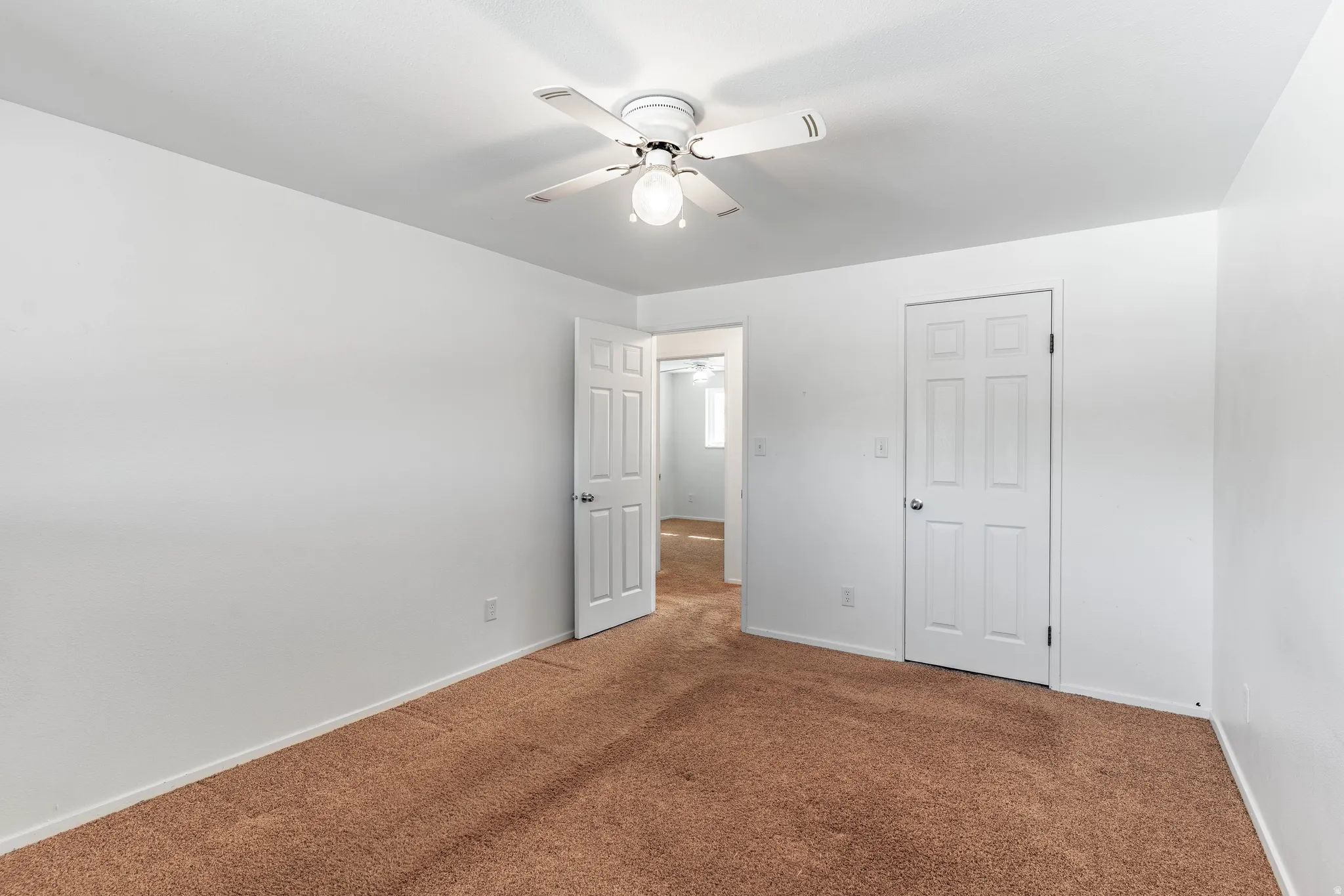 Spacious room featuring neutral white walls and a ceiling fan with integrated lighting