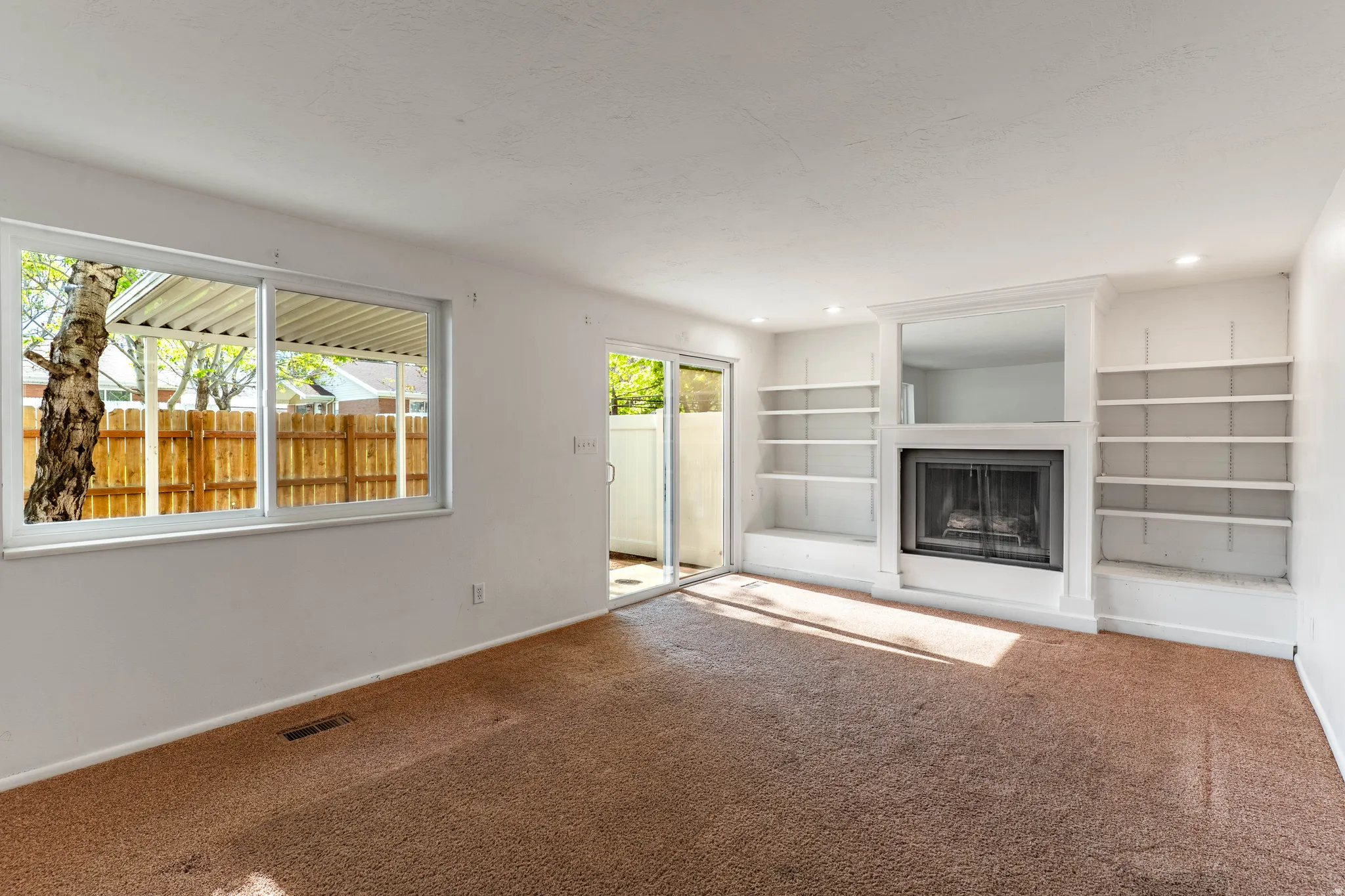 Living area featuring a fireplace with a white mantel, built-in shelving, a sliding glass door, and a window overlooking a wooden fence