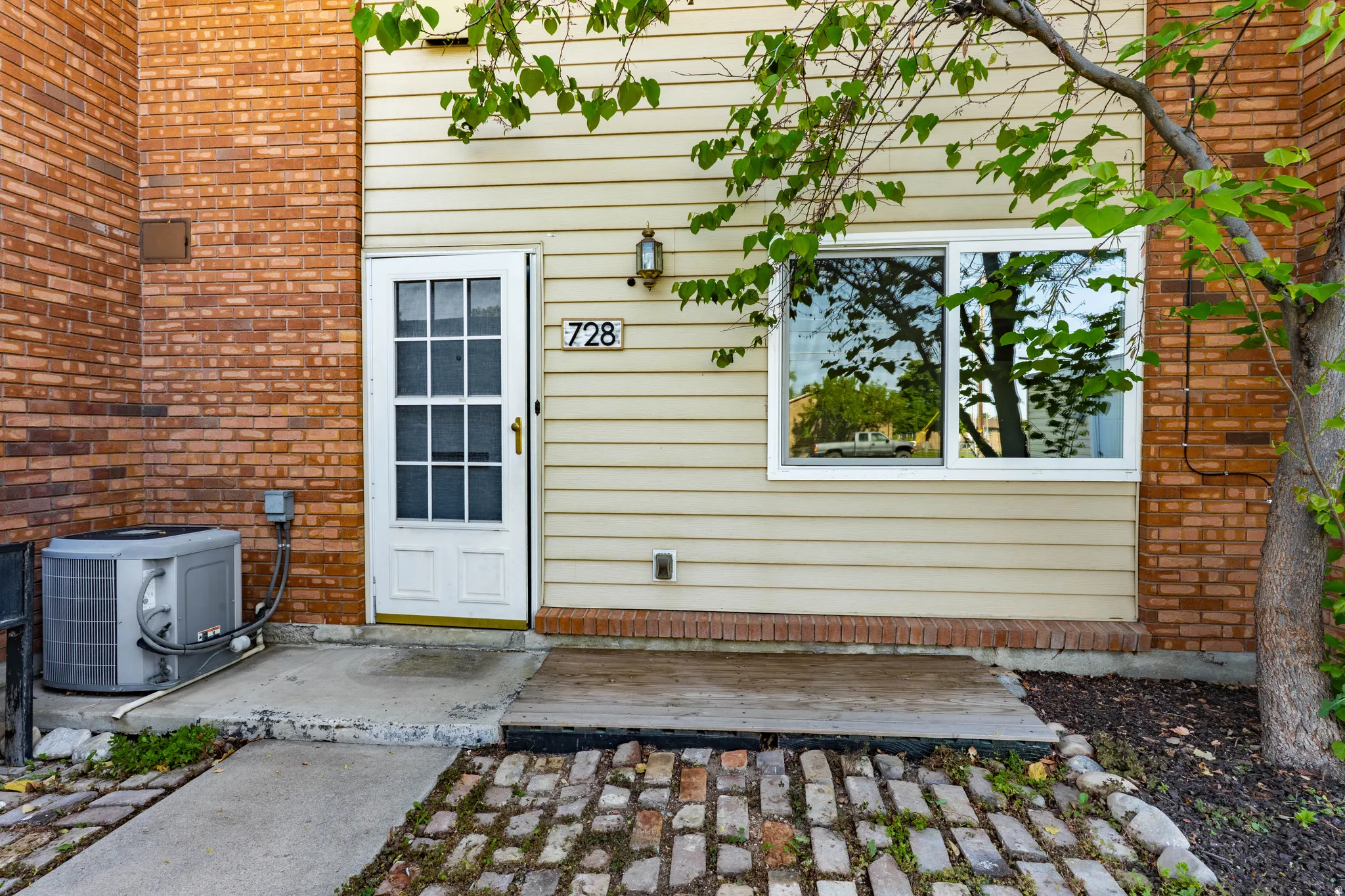 Building exterior featuring brick and horizontal siding, a white entry door with glass panels, a sliding window with white framing, and a paved entry area with a wood landing