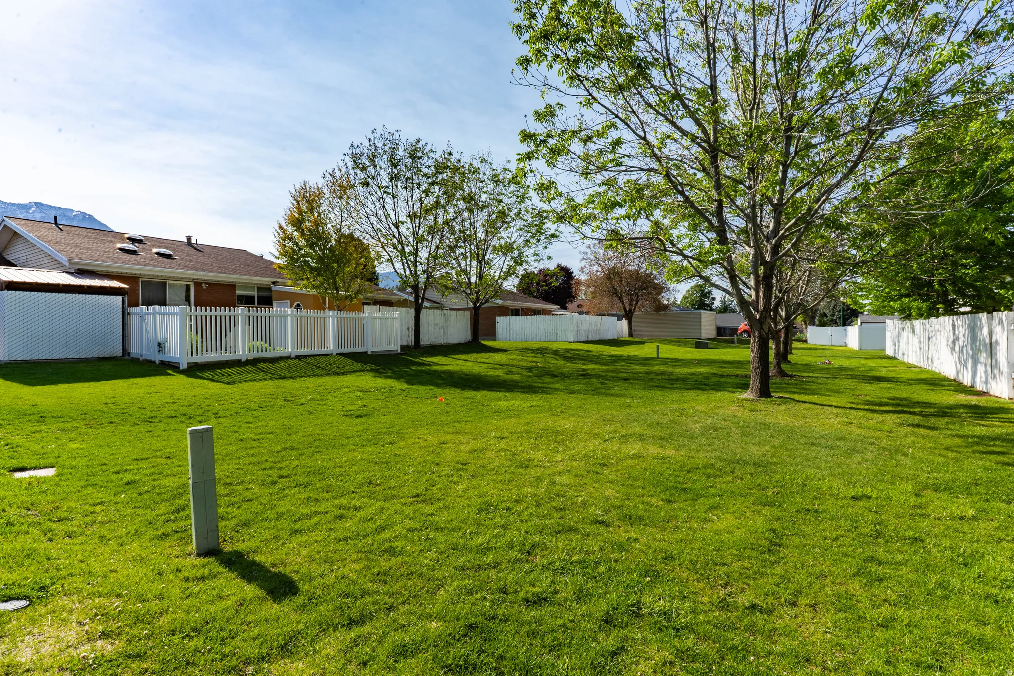 Expansive grass yard bordered by white fencing, featuring mature trees and a distant mountain backdrop