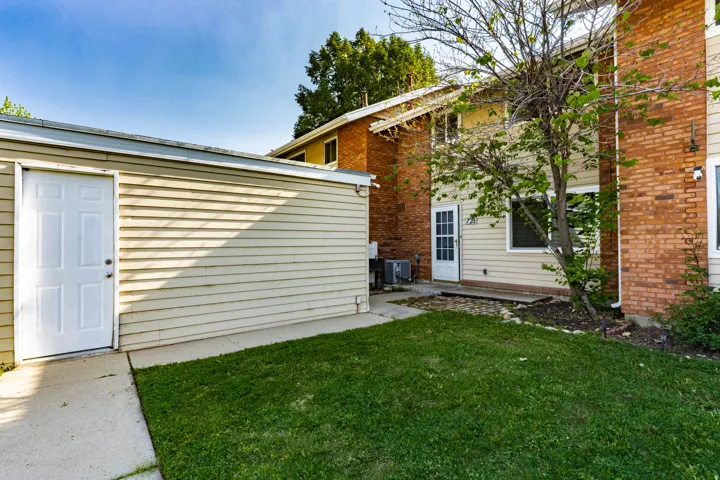 Private outdoor space featuring a detached garage with a white entry door, concrete patio, and lawn area