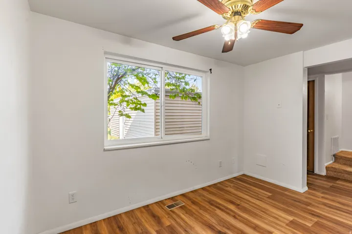 Room featuring wood-finish flooring, a double-pane window, and a ceiling fan with integrated lighting
