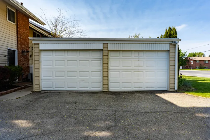 Two-car garage featuring individual panel doors, light-colored siding, and a paved driveway