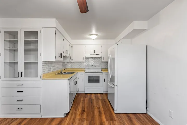 Kitchen featuring white cabinetry with black hardware, glass-front upper cabinets, light yellow countertops, and a subway tile backsplash