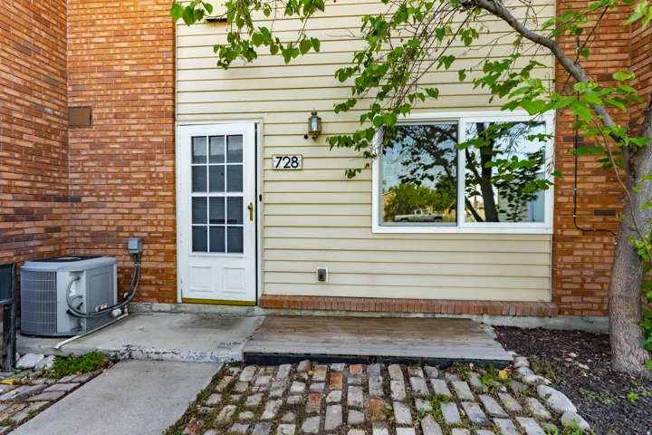 Building exterior featuring brick and horizontal siding, a white entry door with glass panels, a sliding window with white framing, and a paved entry area with a wood landing