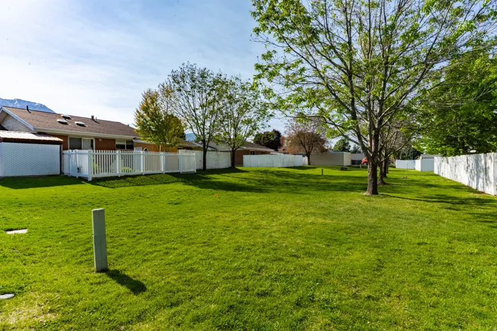 Expansive grass yard bordered by white fencing, featuring mature trees and a distant mountain backdrop