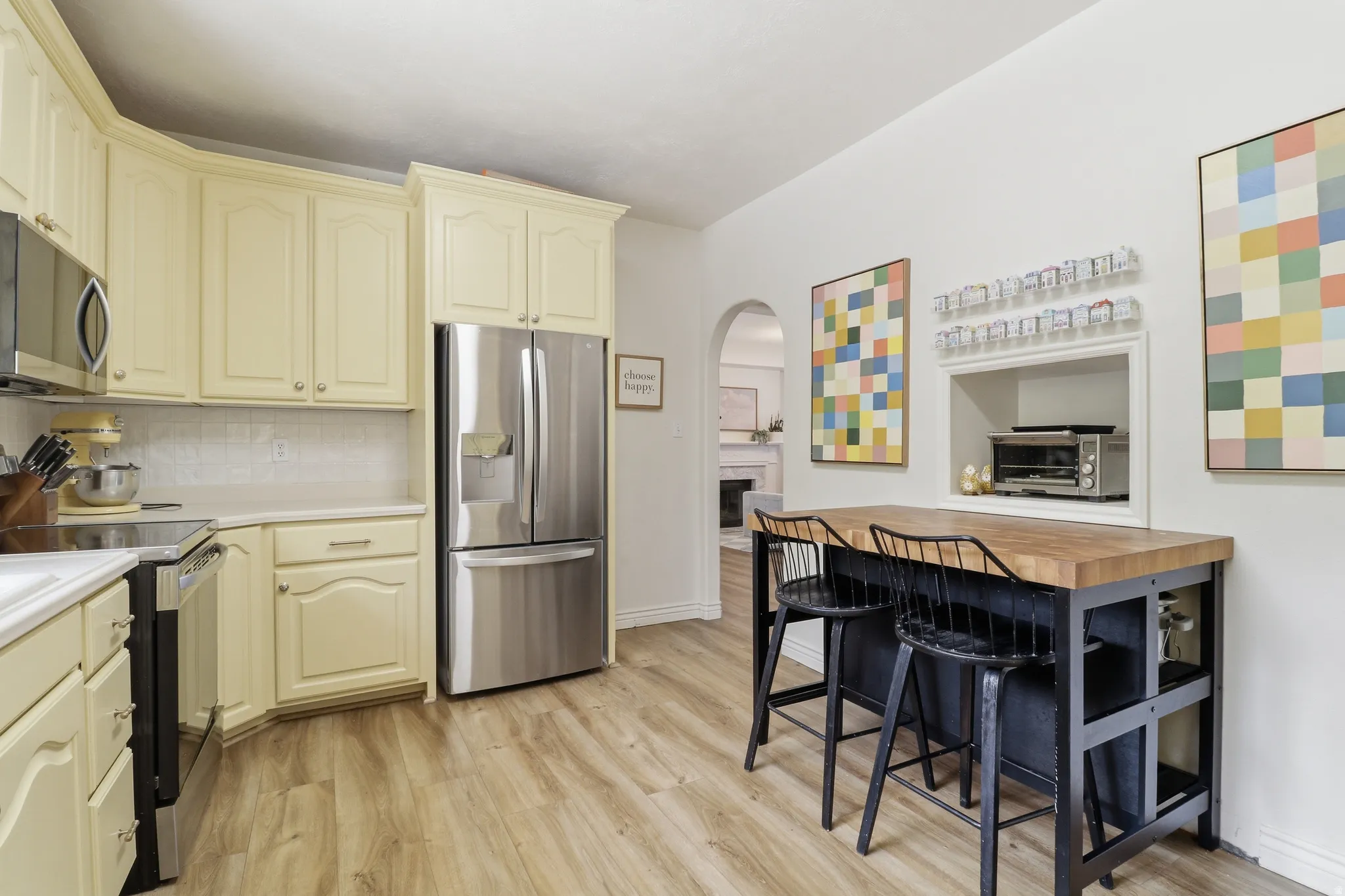 Kitchen featuring light-toned cabinetry, stainless steel appliances, wood-finish flooring, and a butcher block island with seating