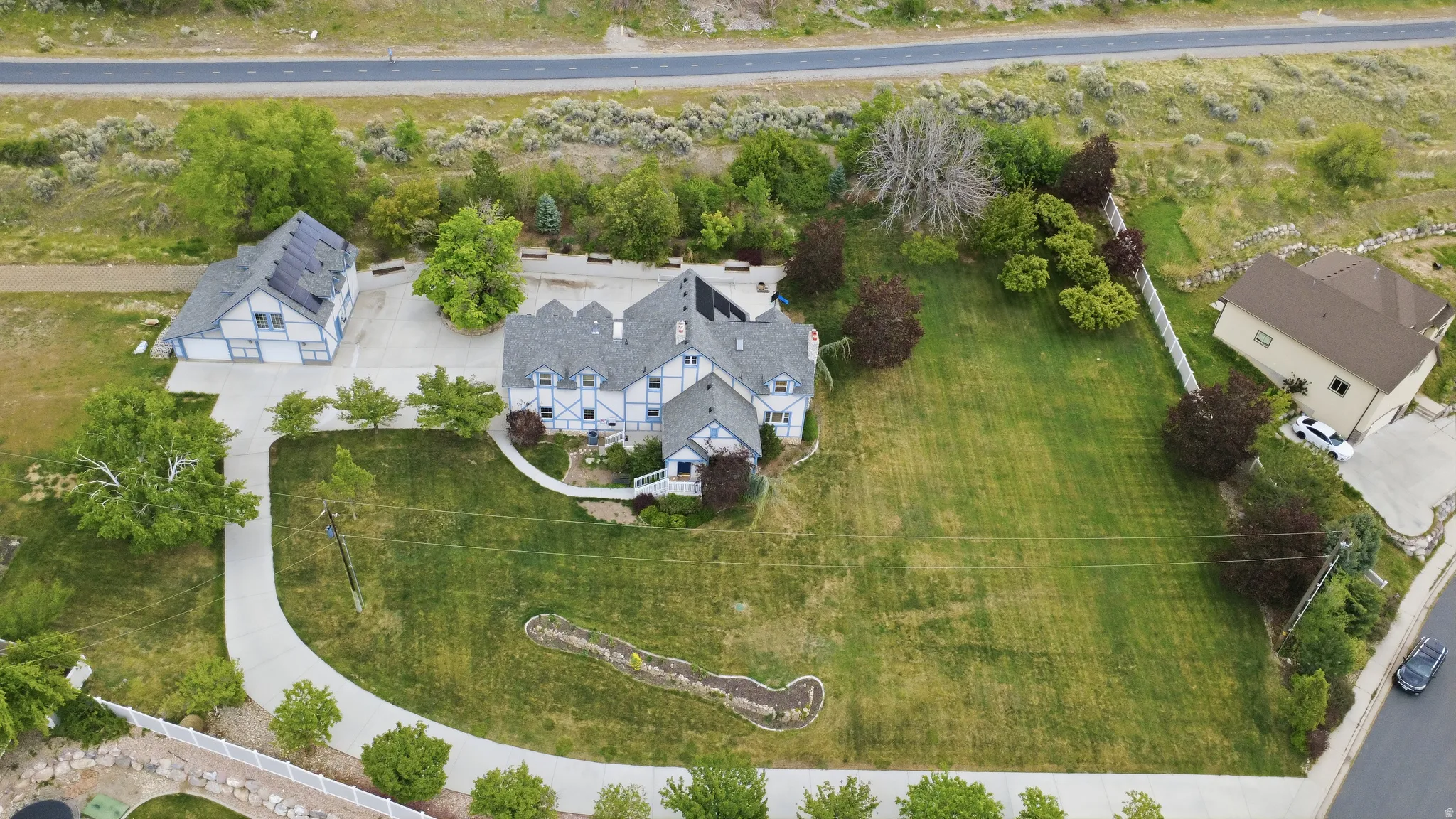 Expansive property featuring a Tudor Revival style main residence with contrasting trim, a separate accessory dwelling unit with rooftop solar panels, a paved driveway, and mature landscaping