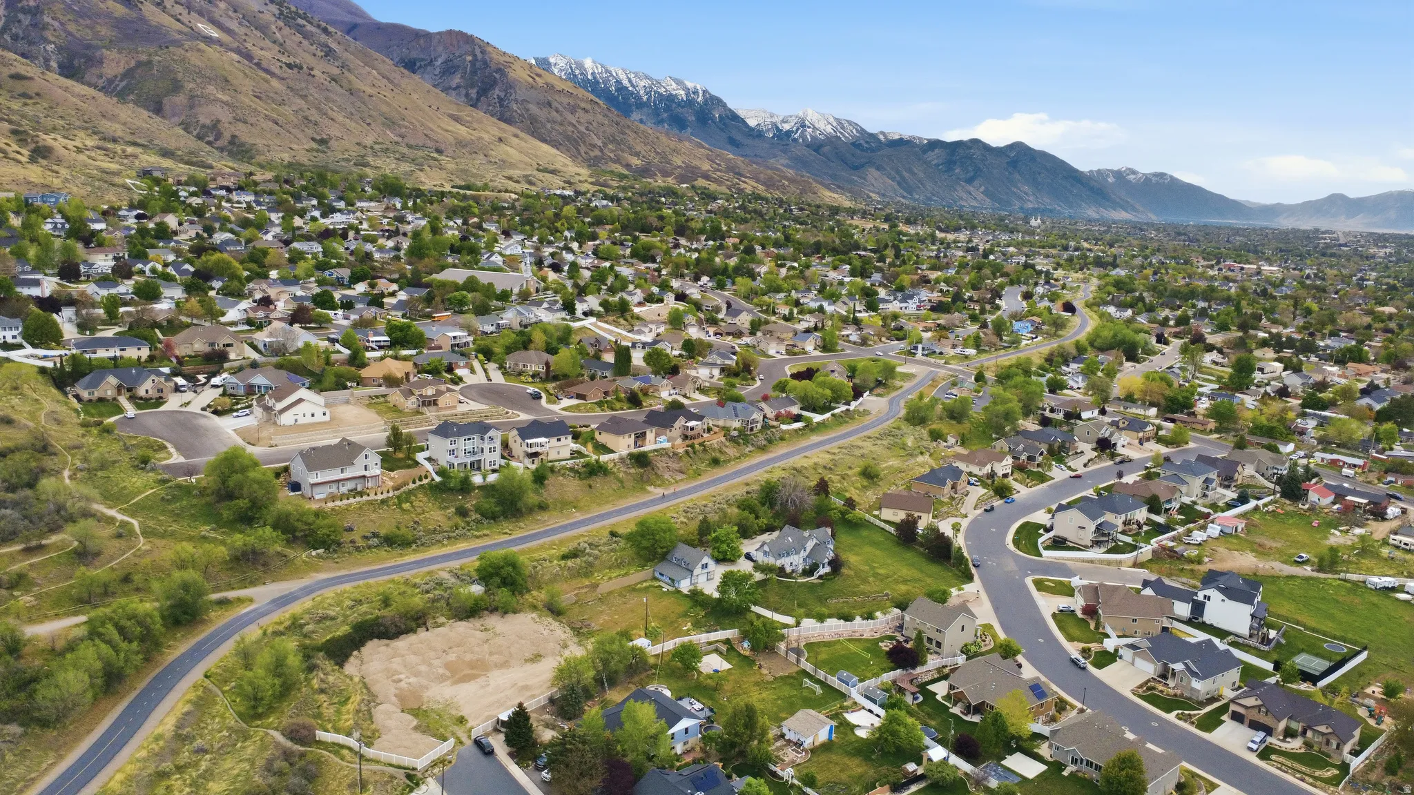 Residential neighborhood with established homes nestled at the base of a mountain range featuring snow-capped peaks