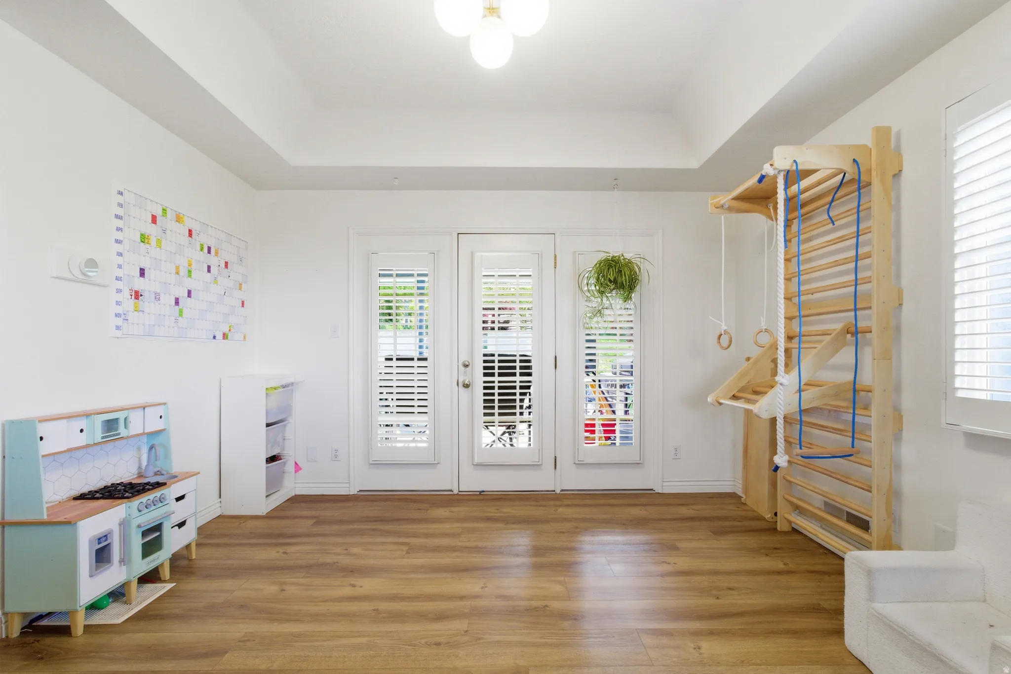 Spacious room with wood-finish flooring, white walls, and a tray ceiling