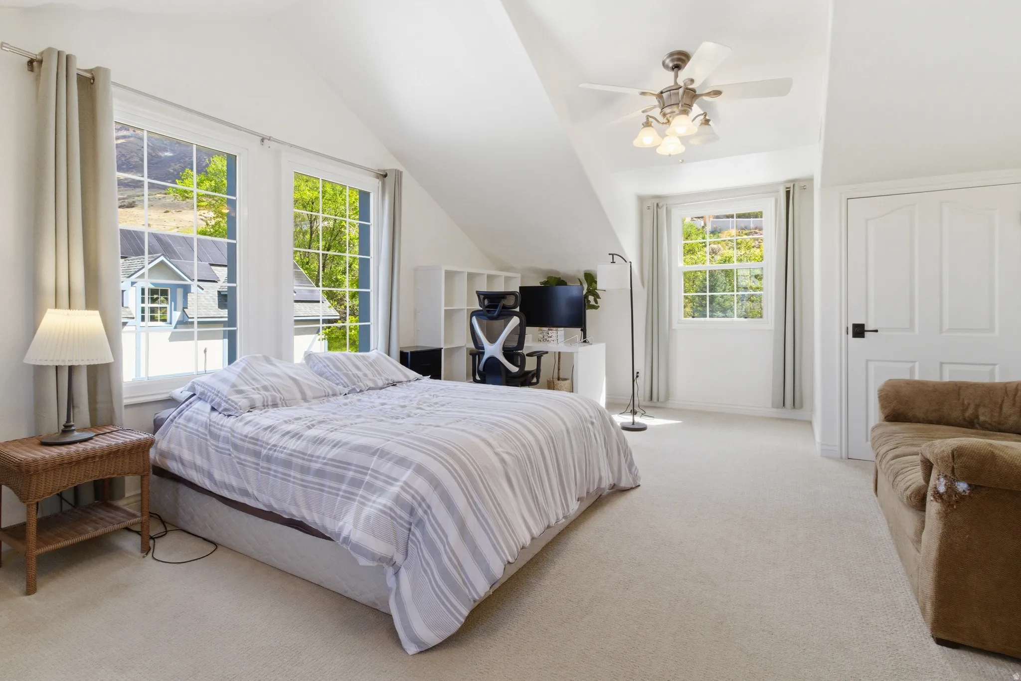 Carpeted room with a vaulted ceiling, featuring multiple windows, a ceiling fan, and a paneled door with black hardware