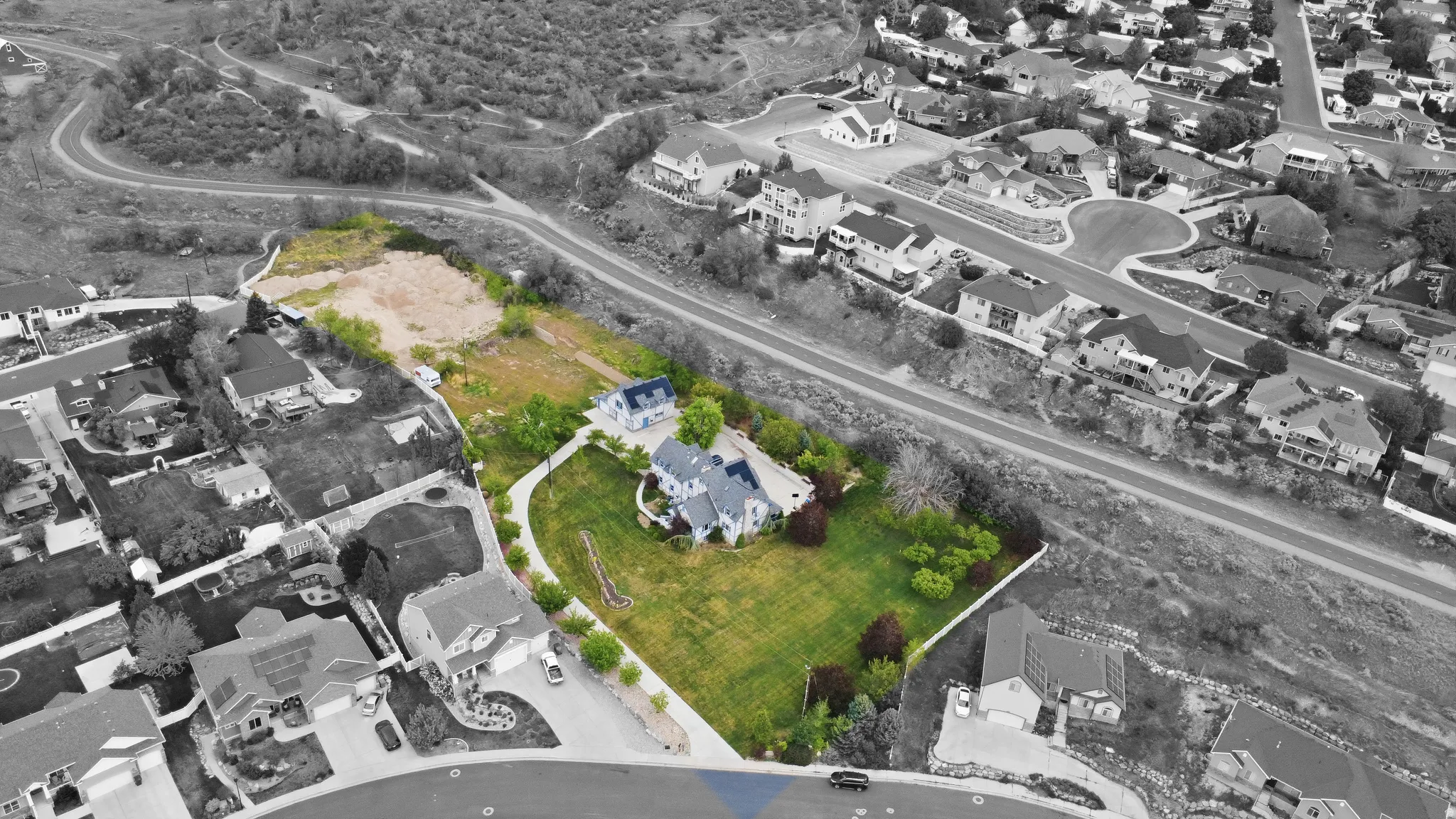 Expansive property featuring a large residence with a manicured green lawn, mature trees, and a paved driveway