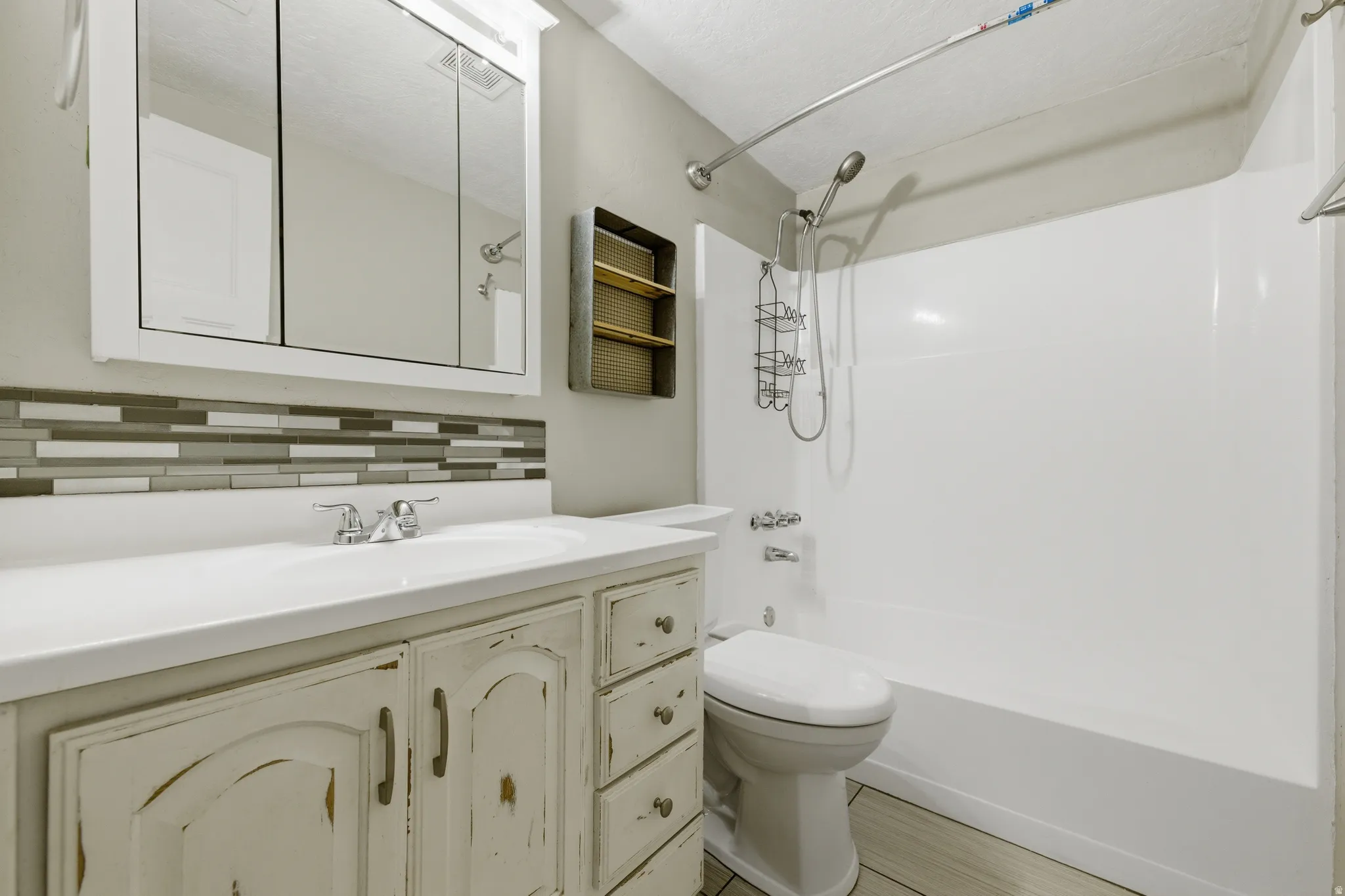 Bathroom featuring a distressed wood-finish vanity with an integrated sink, mosaic tile backsplash, and a medicine cabinet