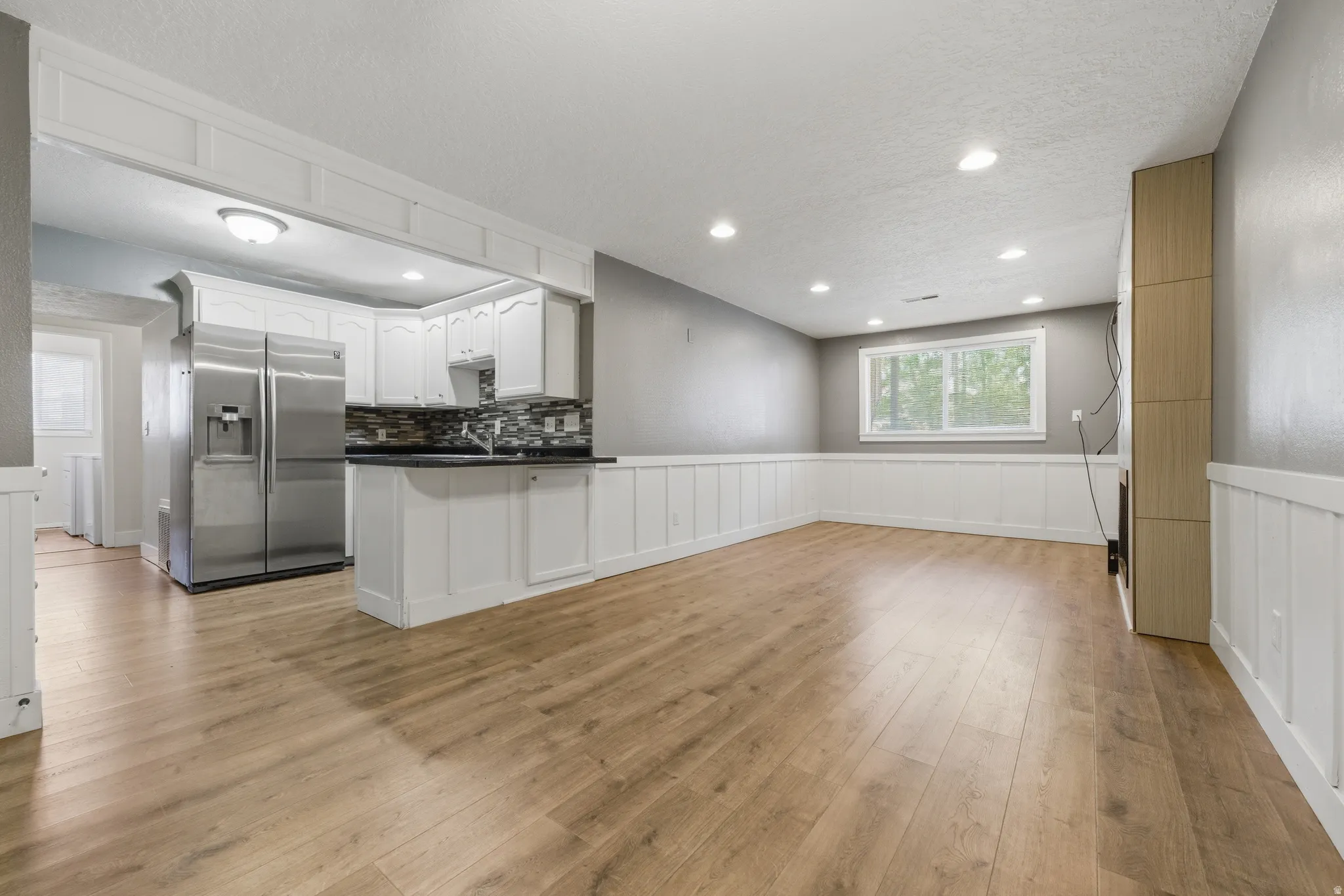 Open-concept living area featuring wood-finish flooring, recessed lighting, and wainscoting