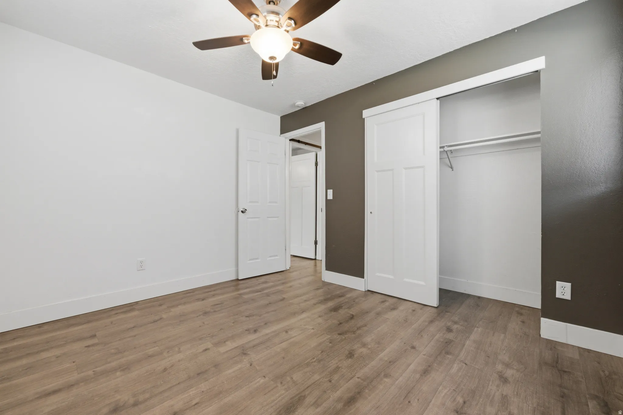 Room featuring wood-finish flooring, a ceiling fan with integrated lighting, and a sliding door closet with internal shelving