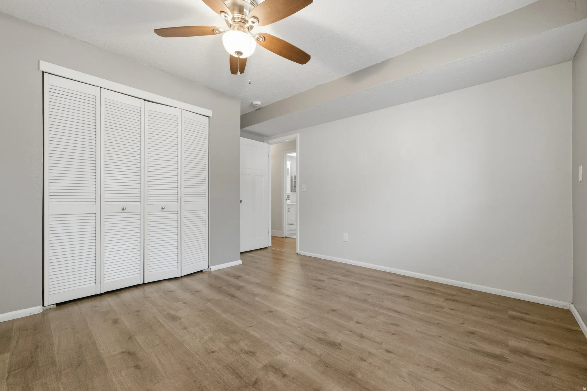 Spacious room featuring wood-finish flooring, light gray walls, and a ceiling fan with integrated lighting