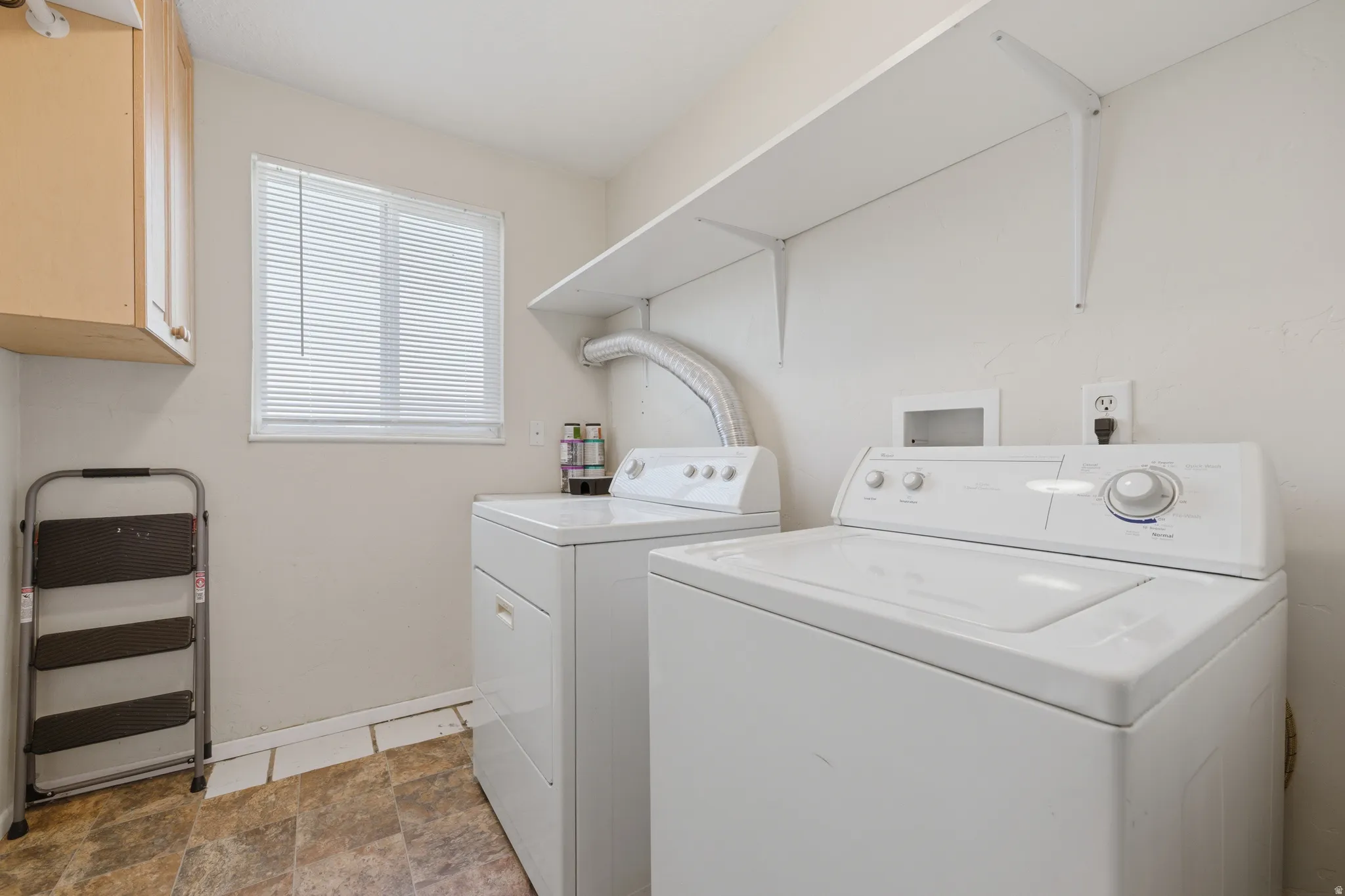Dedicated laundry area featuring a window with blinds, wood-finish cabinetry, built-in shelving, and neutral wall tones