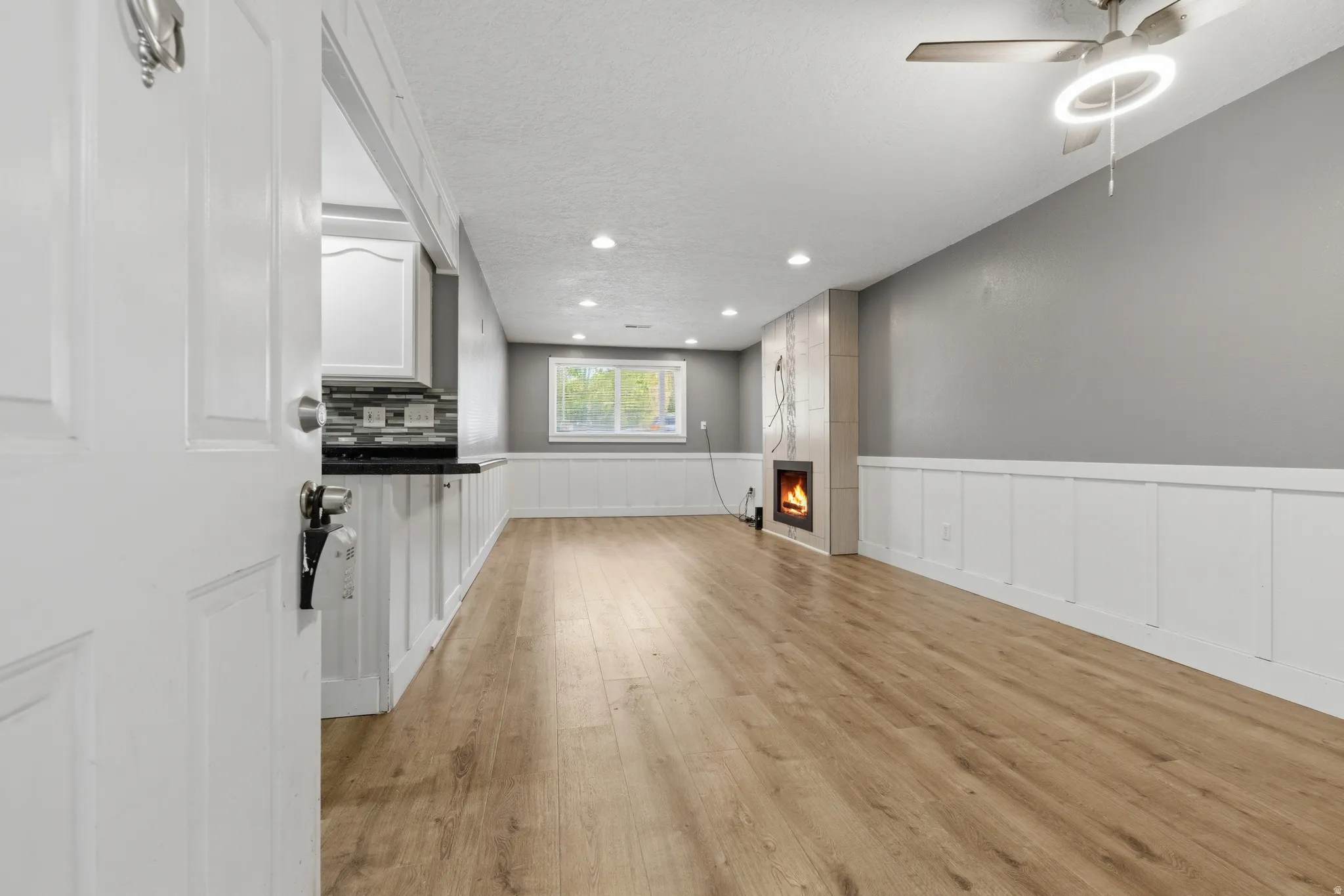 Spacious interior featuring wood-finish flooring, a contemporary electric fireplace with a stacked stone facade, and elegant wainscoting