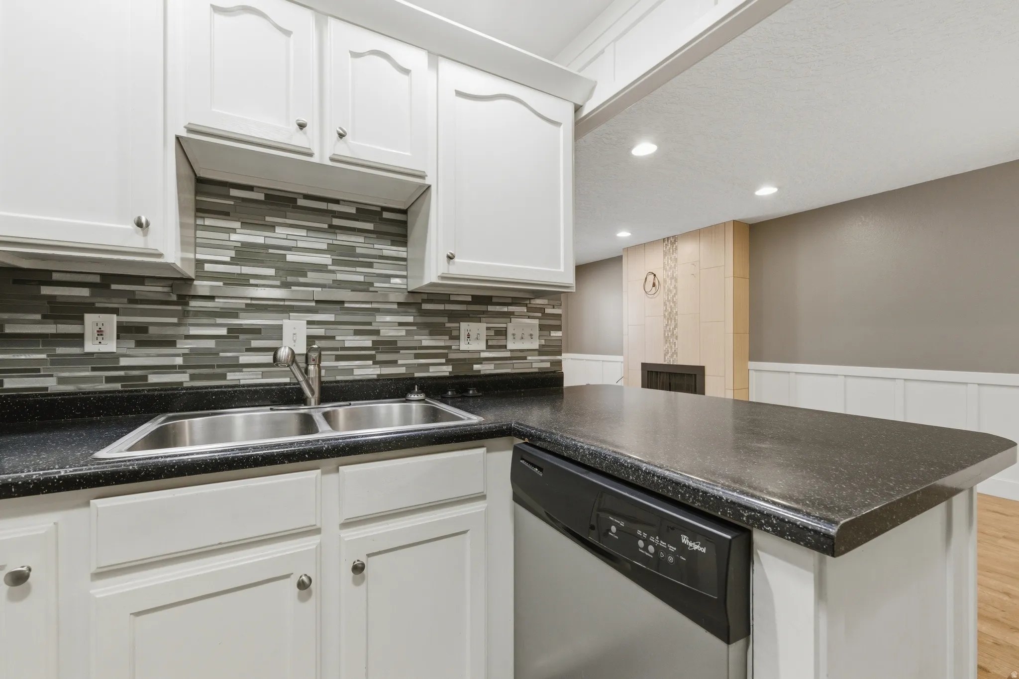 Kitchen featuring white cabinetry, black speckled countertops, a stainless steel double basin sink, mosaic tile backsplash, and an integrated dishwasher